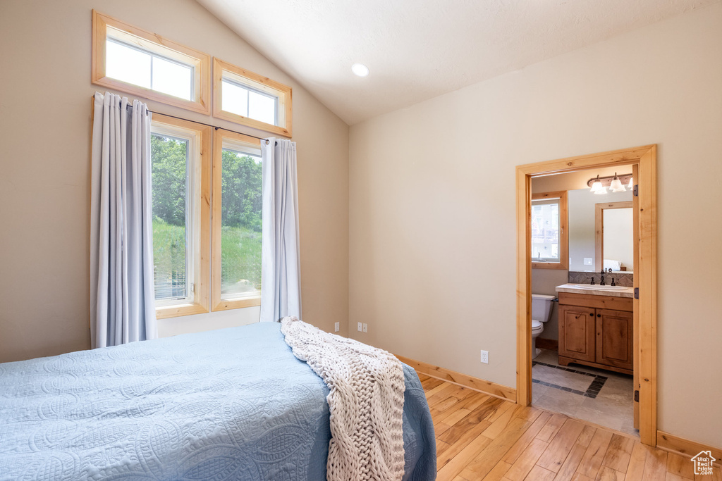 Bedroom featuring vaulted ceiling, light wood-style flooring, and ensuite bath