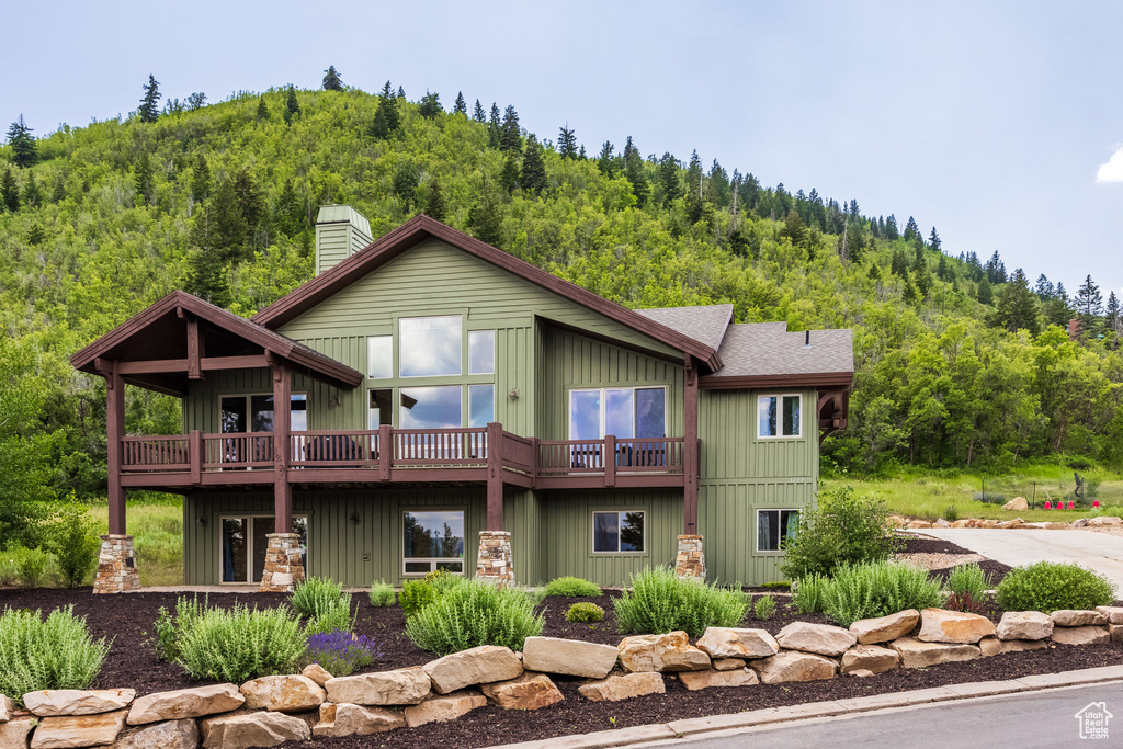 Rear view of property featuring a wooded view, a chimney, a deck, roof with shingles, and board and batten siding