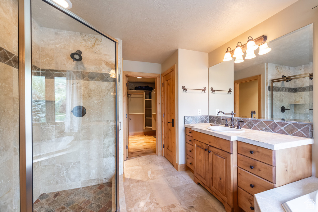 Bathroom with vanity, a shower stall, a spacious closet, backsplash, and a textured ceiling