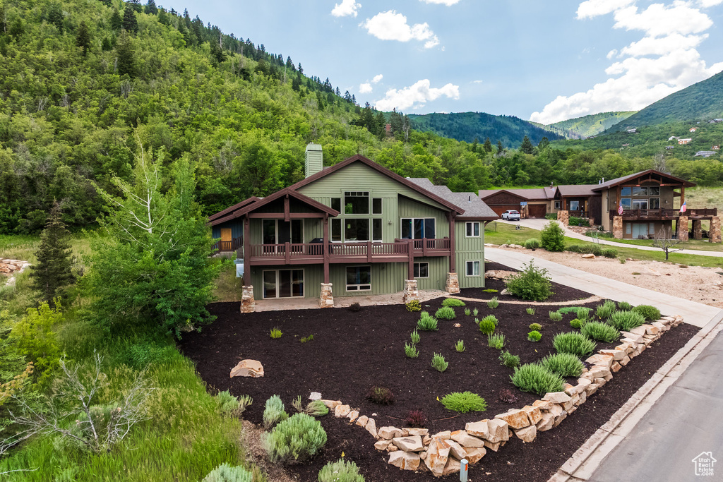 View of front of property featuring a chimney, a deck with mountain view, and a wooded view
