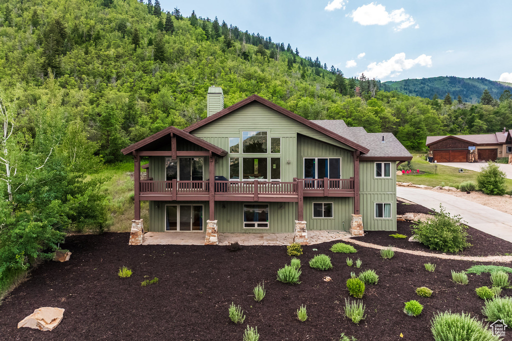Rear view of house featuring a chimney, a view of trees, board and batten siding, a deck with mountain view, and a patio