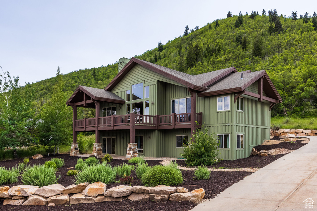Rear view of property featuring a shingled roof, a chimney, and a deck with mountain view