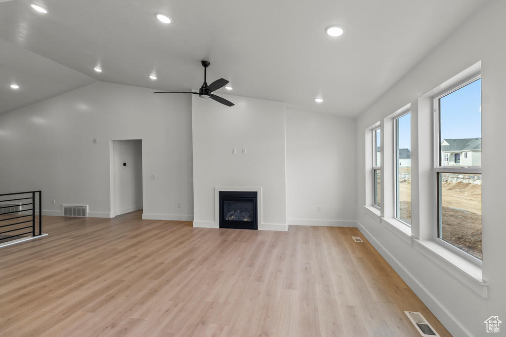 Unfurnished living room featuring light wood finished floors, lofted ceiling, ceiling fan, recessed lighting, and a glass covered fireplace
