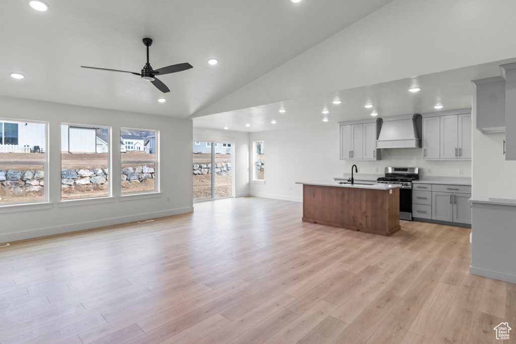 Kitchen with stainless steel stove, custom exhaust hood, open floor plan, ceiling fan, and vaulted ceiling