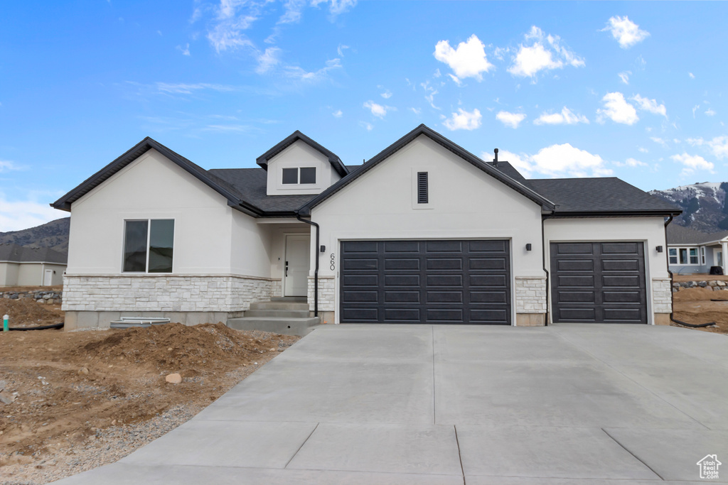 View of front of property with a garage, stone siding, driveway, stucco siding, and a mountain view