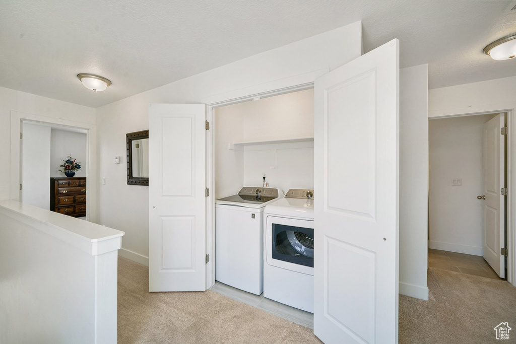 Laundry area with washing machine and dryer, bar with sink, and light colored carpet