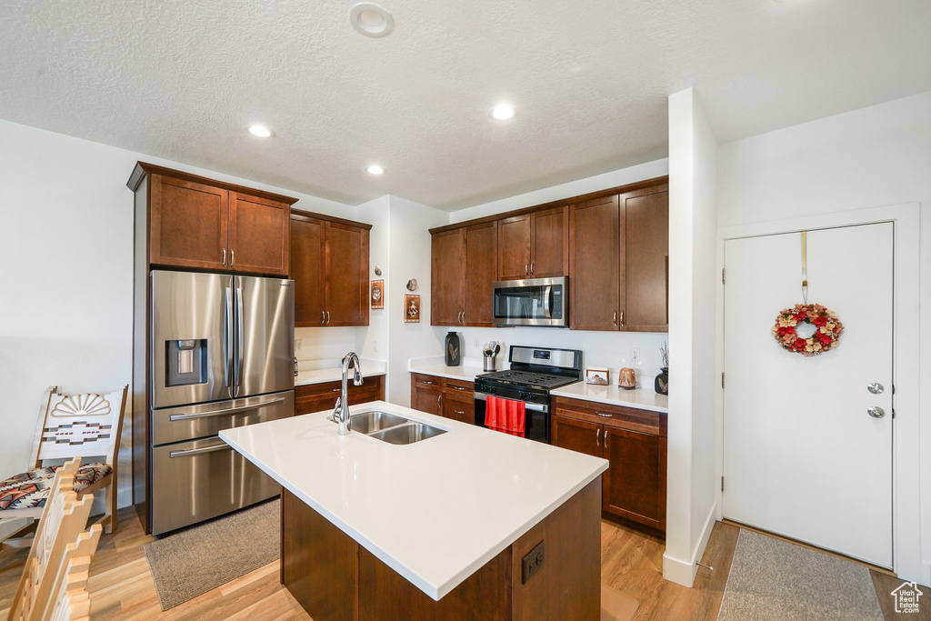 Kitchen with appliances with stainless steel finishes, light wood-style floors, a center island with sink, light countertops, and recessed lighting