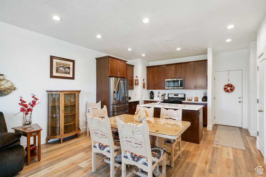 Kitchen with appliances with stainless steel finishes, light countertops, light wood finished floors, a kitchen island with sink, and recessed lighting