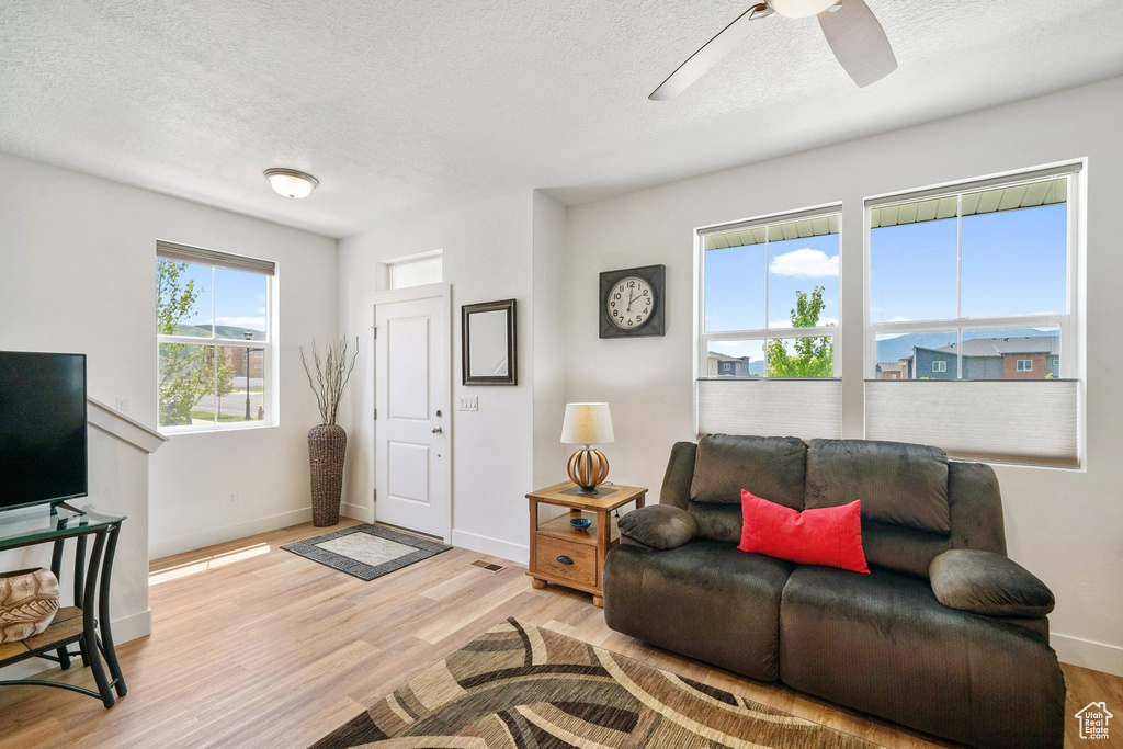 Living room with a textured ceiling, light wood-style floors, and a ceiling fan