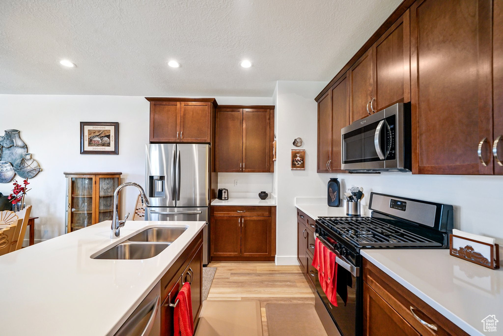 Kitchen with appliances with stainless steel finishes, light countertops, light wood finished floors, recessed lighting, and a textured ceiling