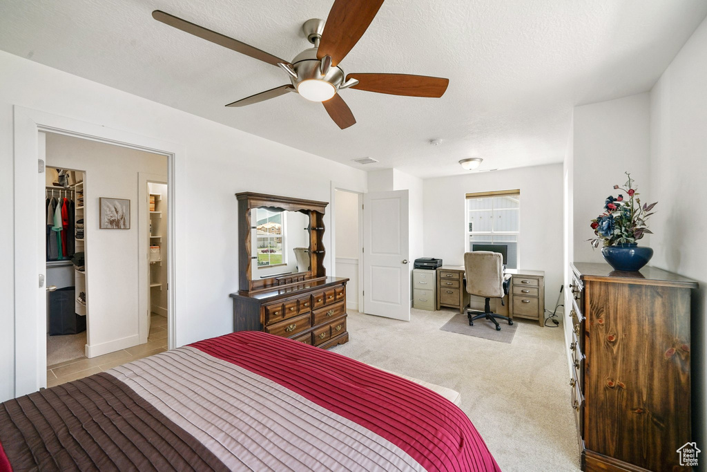 Bedroom with an office area, a walk in closet, light carpet, and a ceiling fan