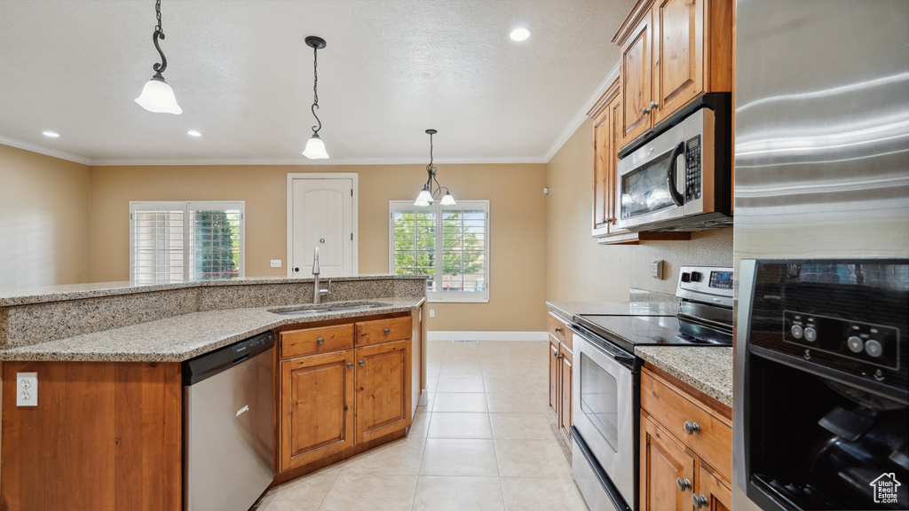 Kitchen featuring appliances with stainless steel finishes, brown cabinets, ornamental molding, decorative light fixtures, and light stone countertops