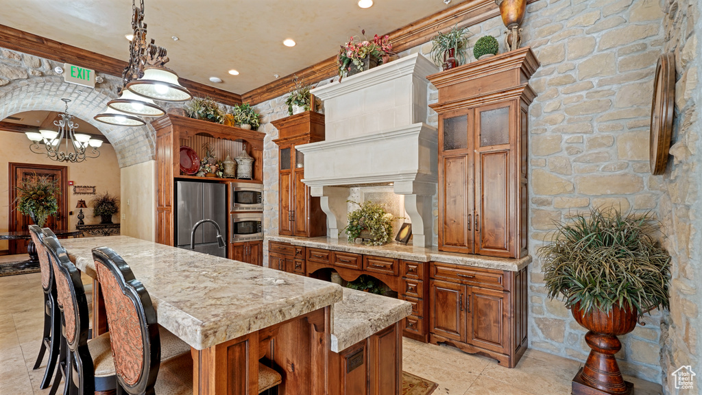 Kitchen featuring appliances with stainless steel finishes, brown cabinets, a chandelier, a center island with sink, and recessed lighting