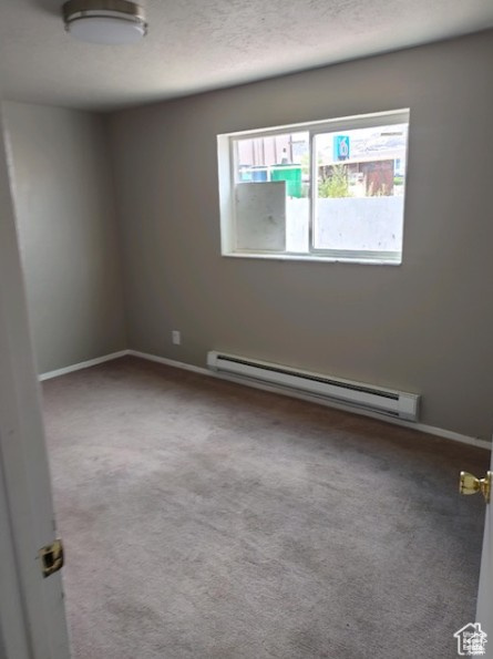 Spare room featuring baseboard heating, carpet flooring, and a textured ceiling