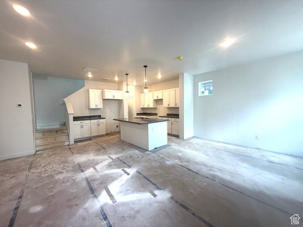 Kitchen featuring dark countertops, a kitchen island, white cabinets, and pendant lighting