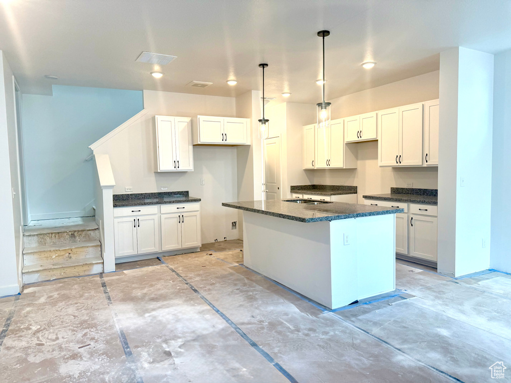 Kitchen with a kitchen island, white cabinetry, dark stone counters, and hanging light fixtures