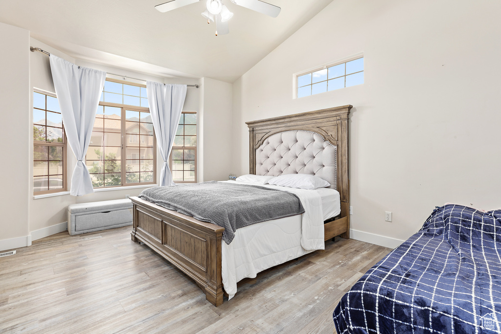 Bedroom with multiple windows, light wood-type flooring, high vaulted ceiling, and a ceiling fan