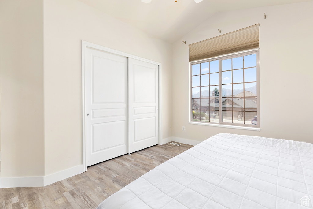 Bedroom with wood finished floors, vaulted ceiling, and a closet