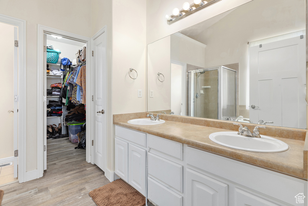 Bathroom with a shower stall, double vanity, a walk in closet, and wood finished floors