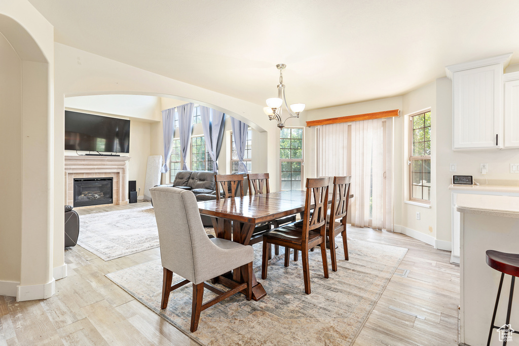 Dining area featuring a chandelier, light wood finished floors, a fireplace, and arched walkways