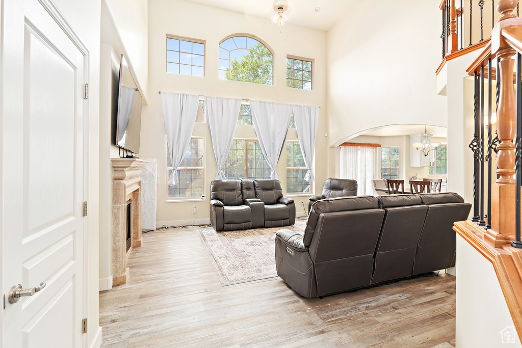 Living area featuring arched walkways, a high ceiling, light wood-type flooring, a chandelier, and healthy amount of natural light