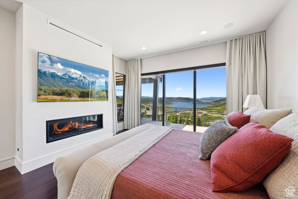 Bedroom featuring wood finished floors, a glass covered fireplace, a water and mountain view, recessed lighting, and access to exterior