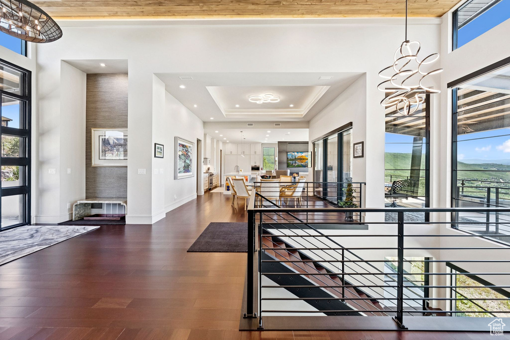 Foyer with plenty of natural light, wood finished floors, a tray ceiling, a chandelier, and a towering ceiling