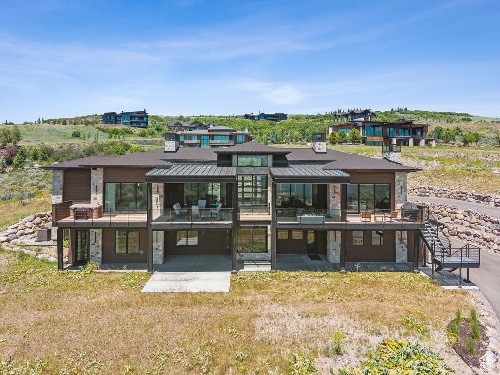 Back of house with stone siding, a standing seam roof, a metal roof, and a patio area