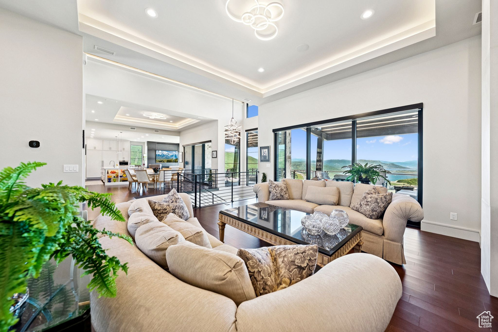 Living room with a tray ceiling, a chandelier, wood finished floors, and recessed lighting