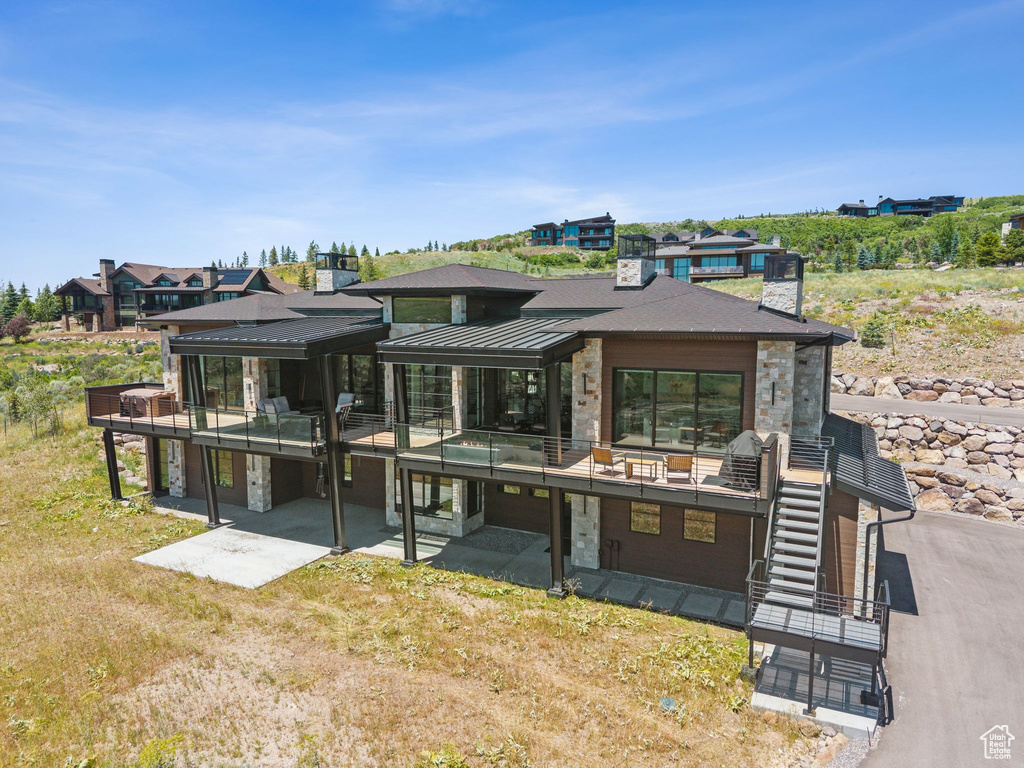 Rear view of property featuring stone siding, a patio area, stairway, and a standing seam roof