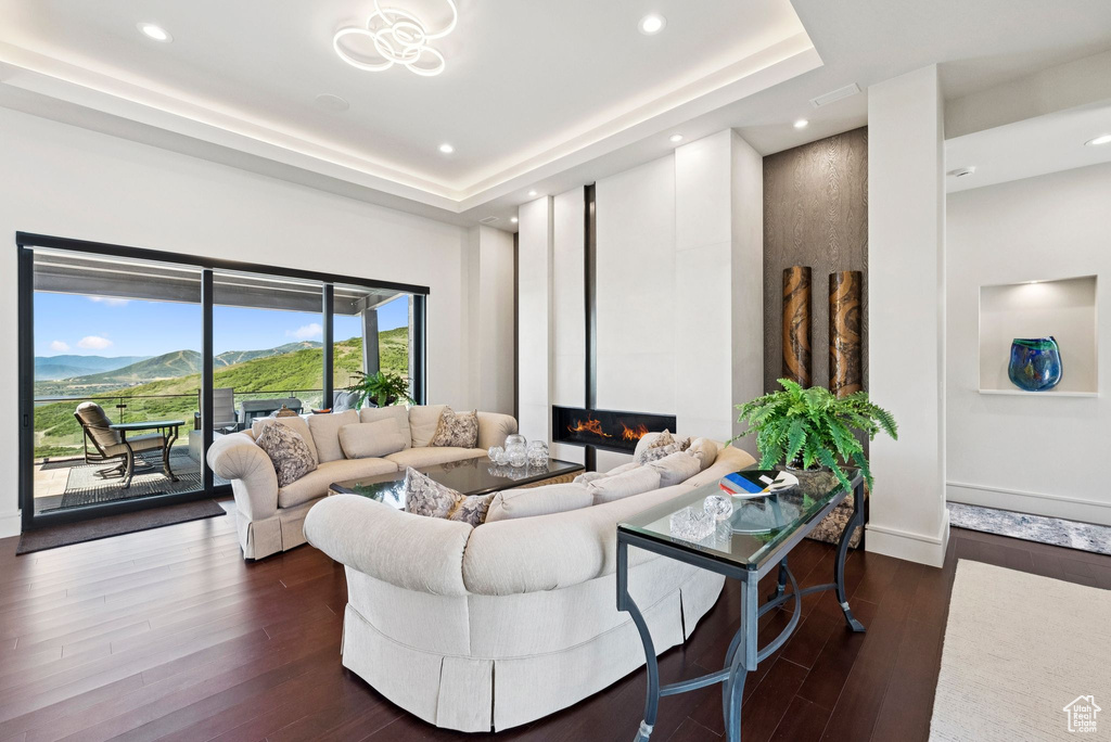 Living room featuring dark wood finished floors, a glass covered fireplace, recessed lighting, and a raised ceiling