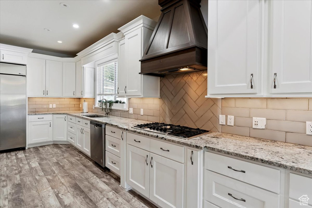 Kitchen with appliances with stainless steel finishes, premium range hood, white cabinets, and recessed lighting