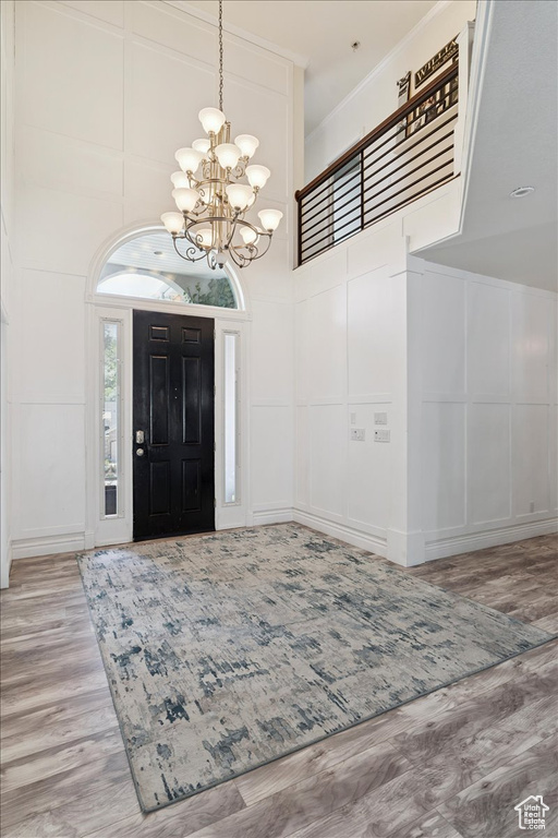 Foyer entrance featuring a decorative wall, a chandelier, wood finished floors, a high ceiling, and crown molding
