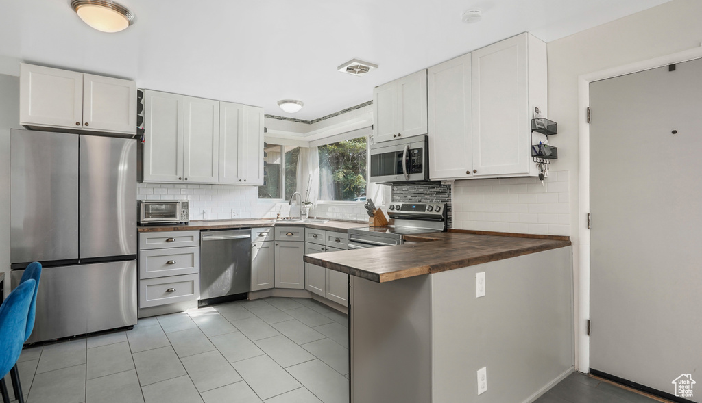 Kitchen featuring appliances with stainless steel finishes, a peninsula, decorative backsplash, light tile patterned flooring, and wood counters