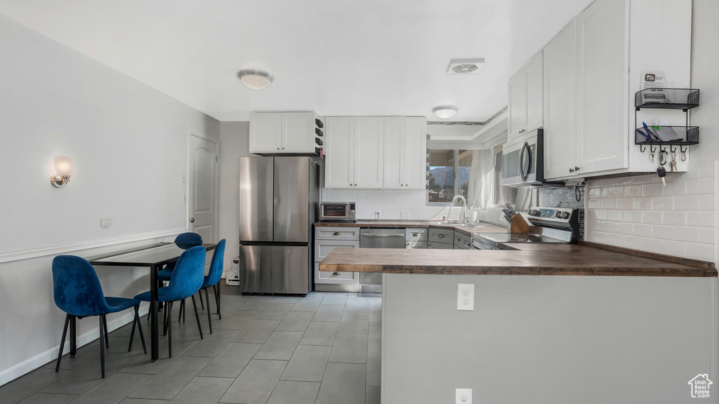 Kitchen with stainless steel appliances, decorative backsplash, white cabinets, and a peninsula