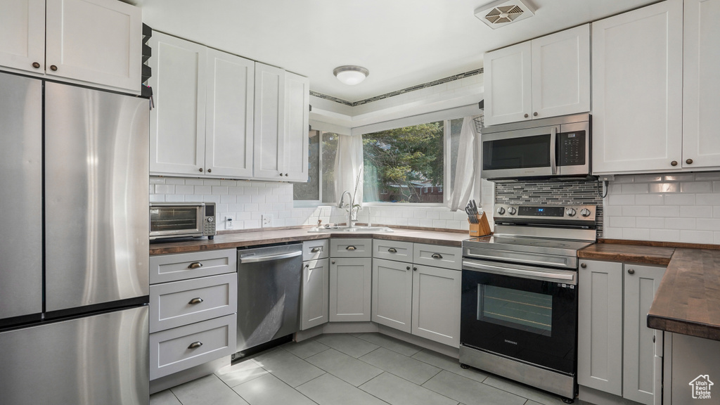 Kitchen with stainless steel appliances, butcher block counters, light tile patterned floors, and backsplash