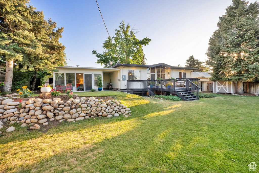 Rear view of property featuring a sunroom, a wooden deck, a yard, and a shed