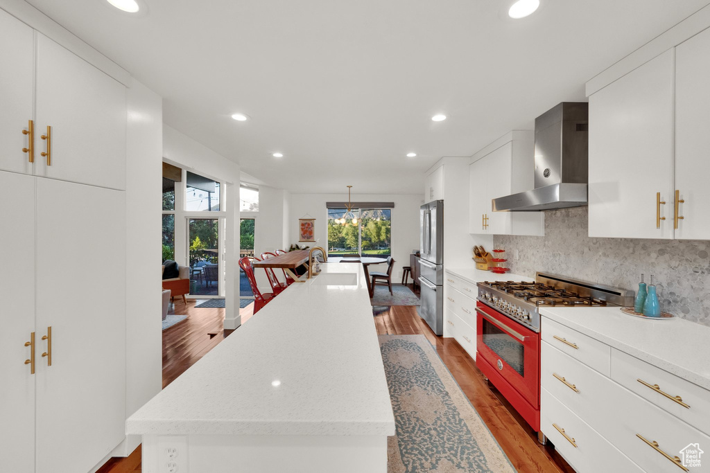 Kitchen with appliances with stainless steel finishes, wall chimney exhaust hood, an island with sink, light wood-style floors, and recessed lighting