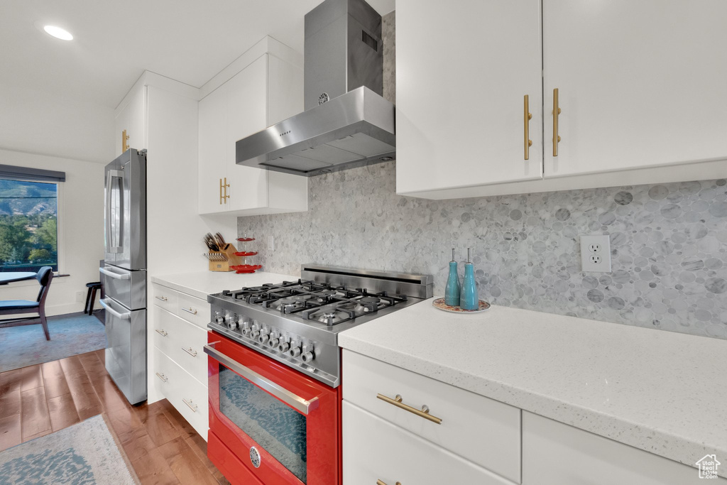 Kitchen with stainless steel appliances, wall chimney range hood, light wood-style flooring, decorative backsplash, and white cabinetry