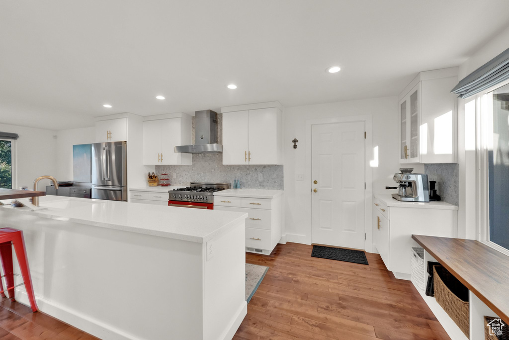Kitchen featuring wall chimney range hood, stainless steel appliances, tasteful backsplash, light countertops, and glass insert cabinets