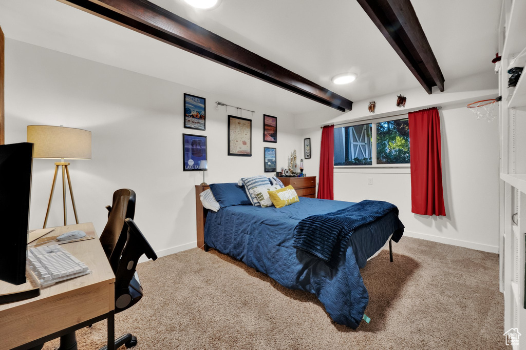 Carpeted bedroom featuring beam ceiling and a desk