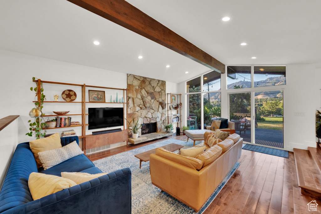 Living room featuring beamed ceiling, wood finished floors, a stone fireplace, recessed lighting, and high vaulted ceiling