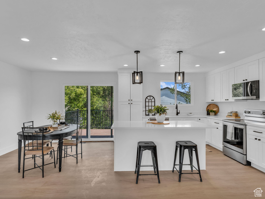 Kitchen featuring appliances with stainless steel finishes, recessed lighting, a center island, a breakfast bar area, and white cabinets