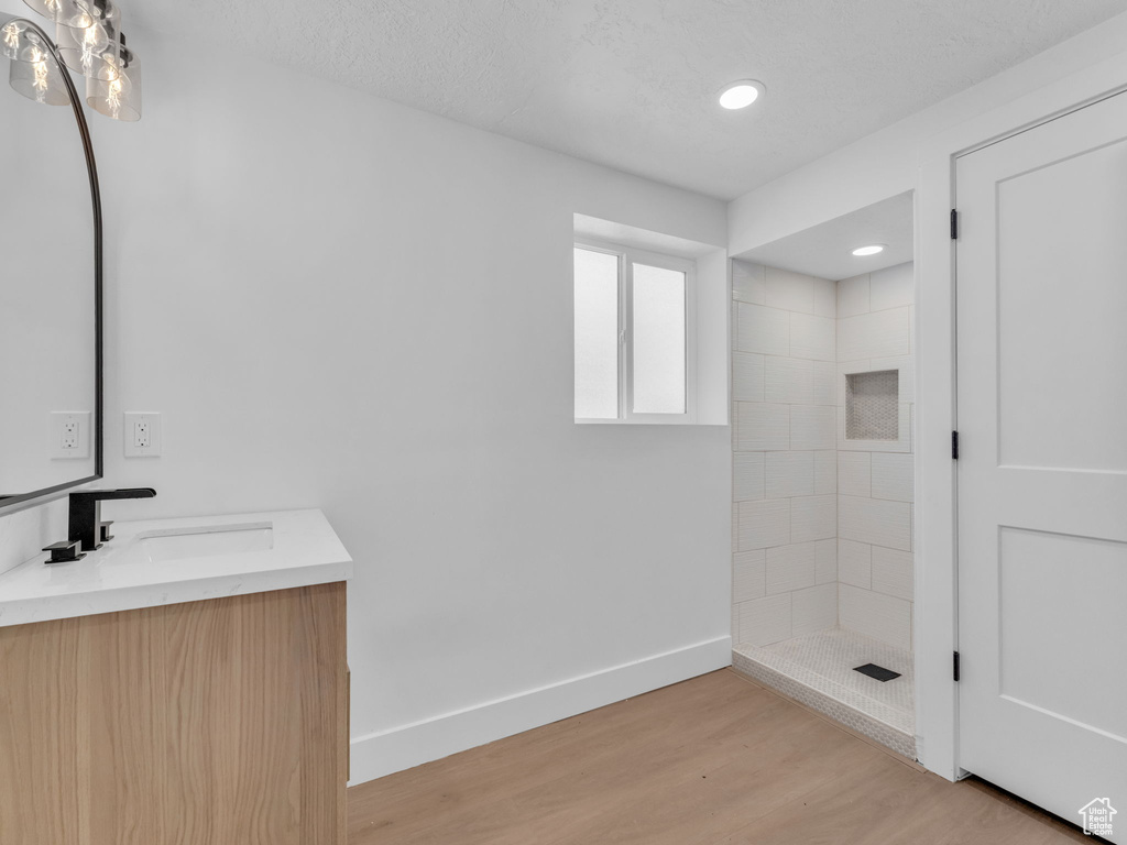Bathroom with vanity, a tile shower, wood finished floors, and recessed lighting