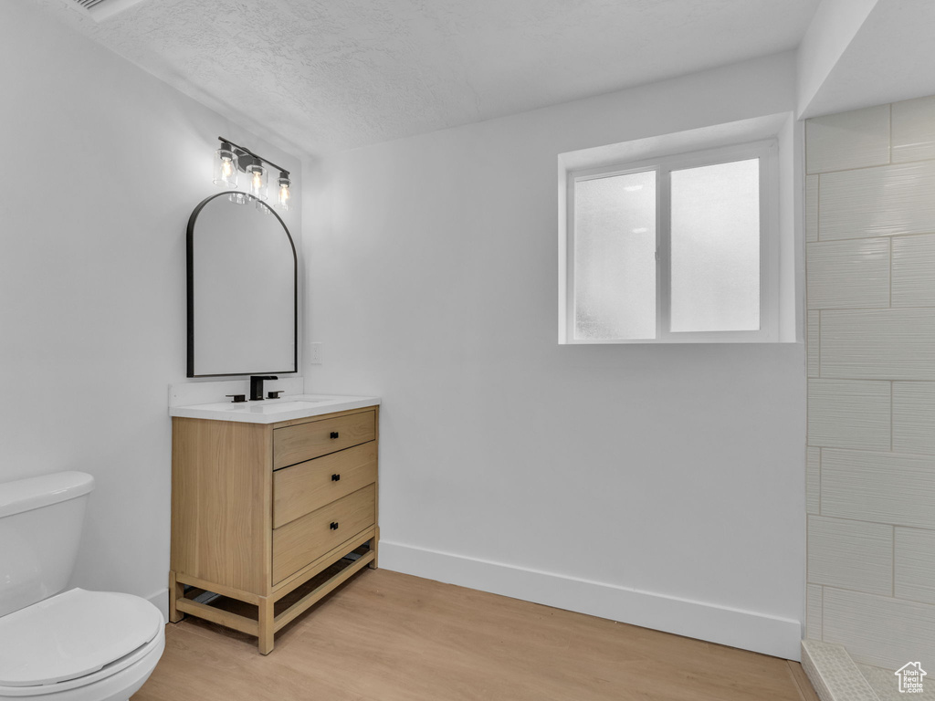Full bath featuring wood finished floors, vanity, tiled shower, and a textured ceiling