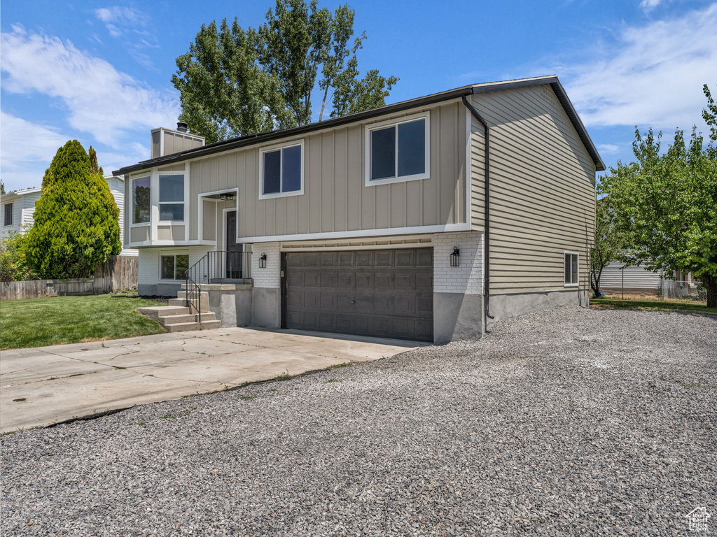 Raised ranch with driveway, an attached garage, a chimney, and brick siding