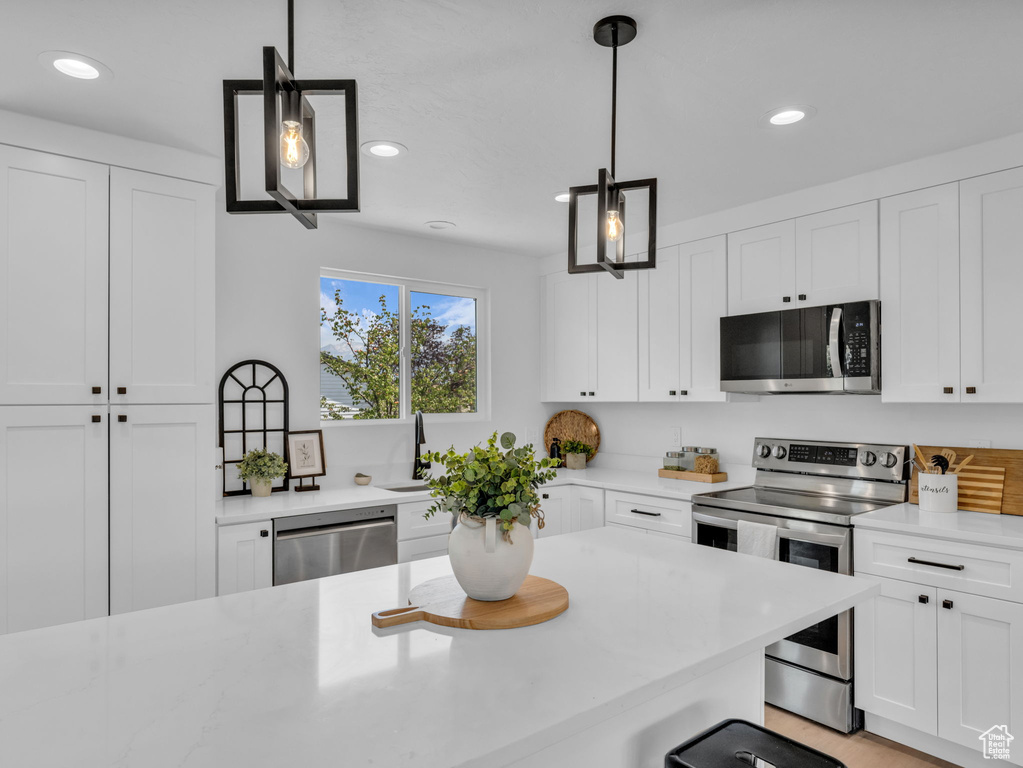 Kitchen featuring appliances with stainless steel finishes, recessed lighting, white cabinets, and decorative light fixtures