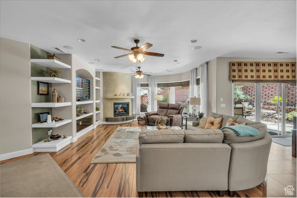 Living area featuring a ceiling fan, healthy amount of natural light, built in shelves, a glass covered fireplace, and recessed lighting