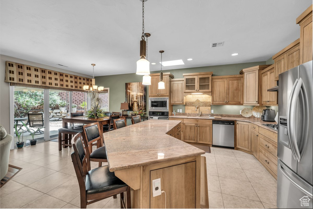 Kitchen with appliances with stainless steel finishes, a center island, decorative backsplash, a kitchen breakfast bar, and light tile patterned floors