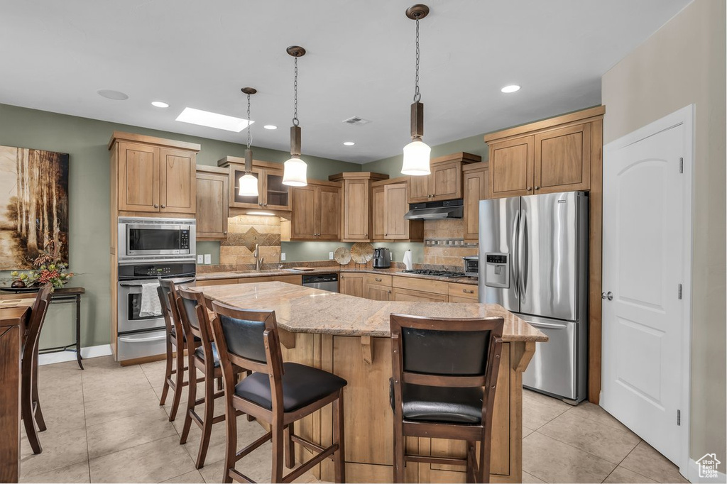 Kitchen featuring appliances with stainless steel finishes, under cabinet range hood, decorative backsplash, light stone countertops, and recessed lighting
